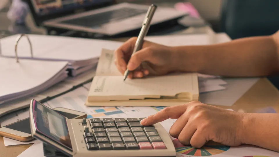 Hands using a calculator and writing in a notebook at a desk