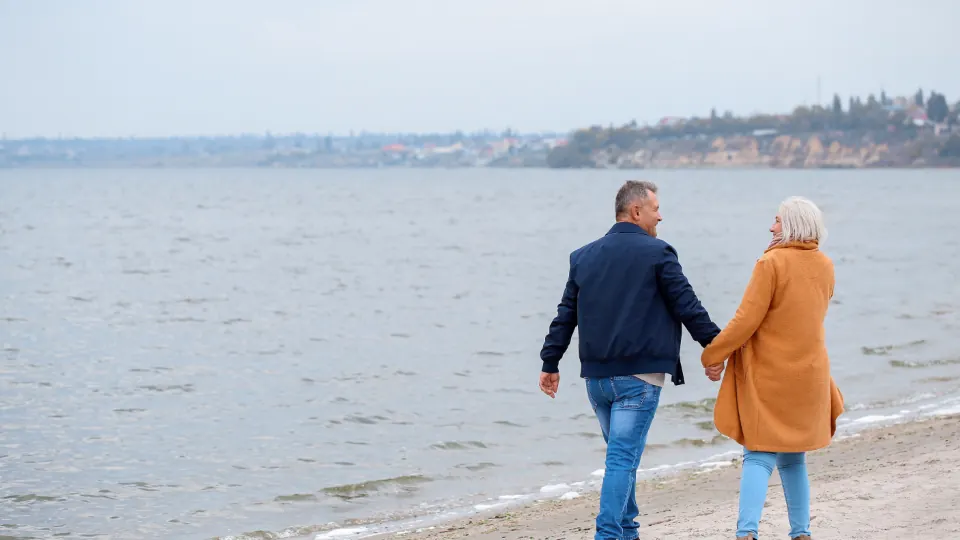Older couple walking along a beach, seen from behind