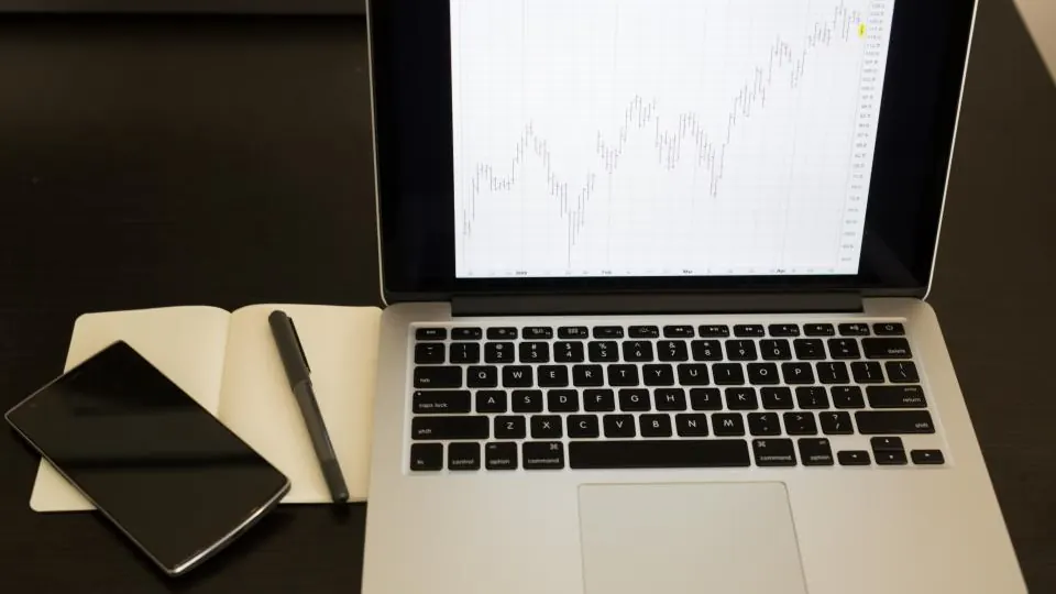 Laptop showing a line chart next to a notebook and phone