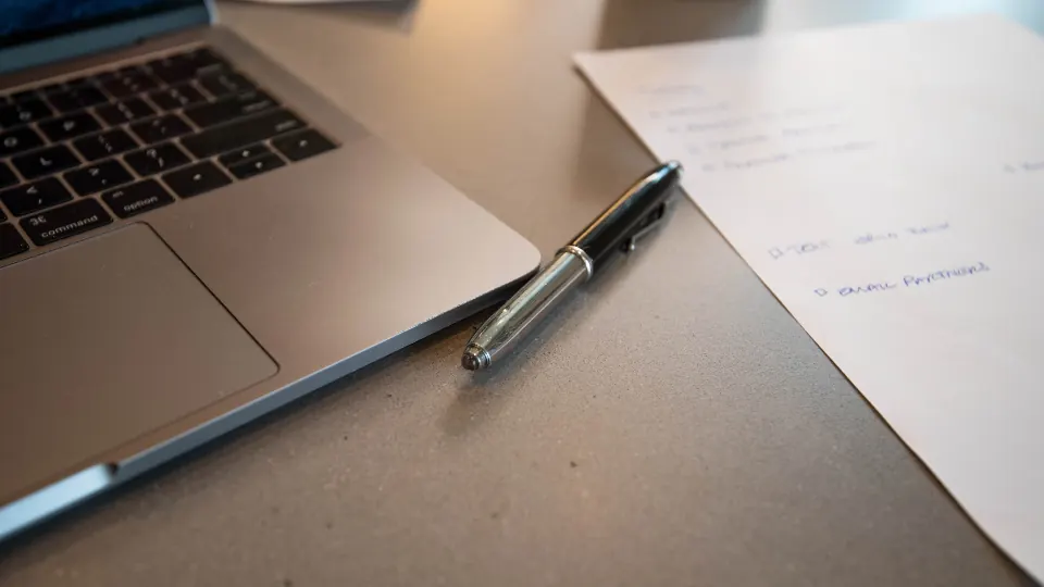 Laptop and a printed page with a pen on a desk