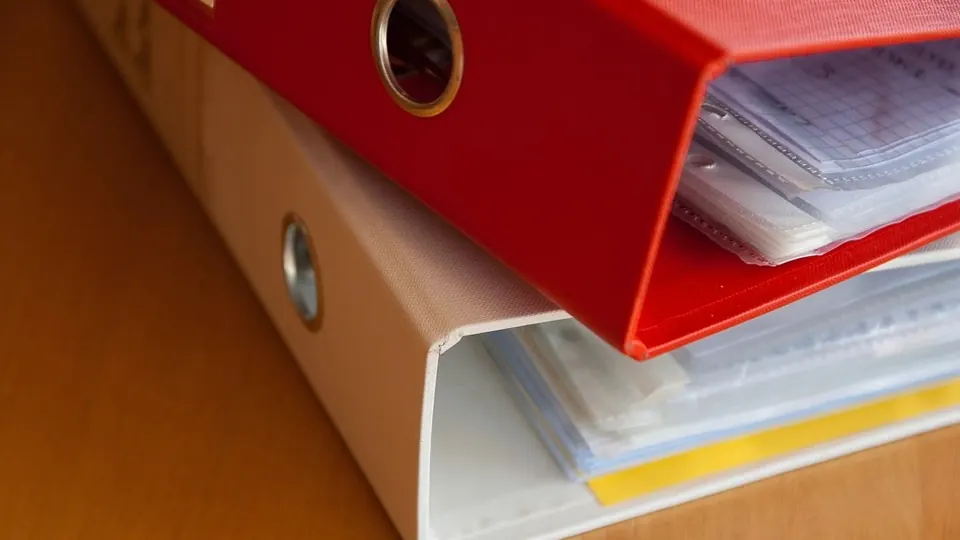 Red ring binder full of papers on a wooden desk