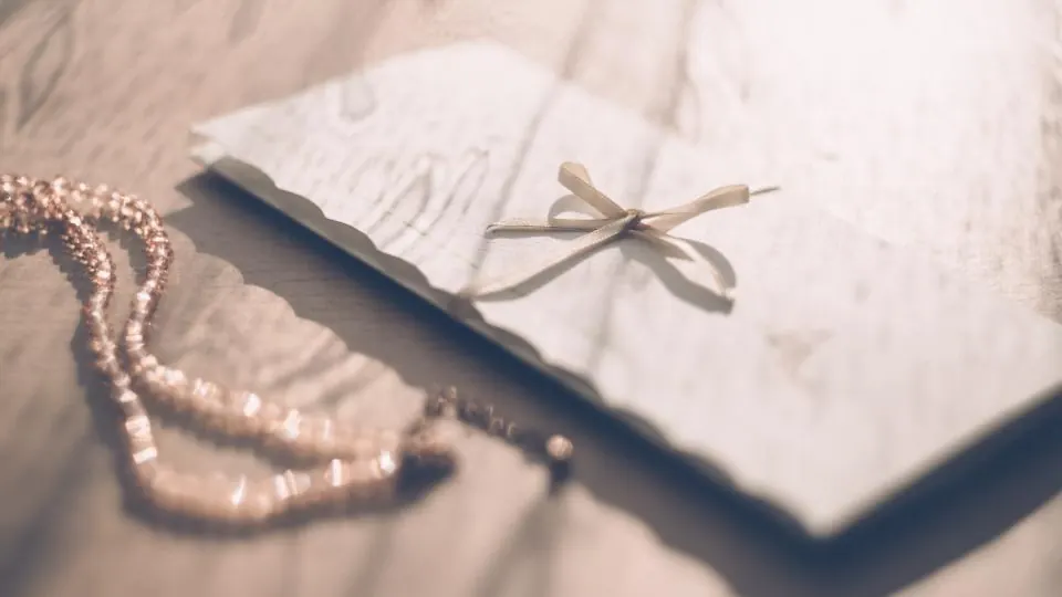 Envelope tied with a ribbon next to a string of pearls